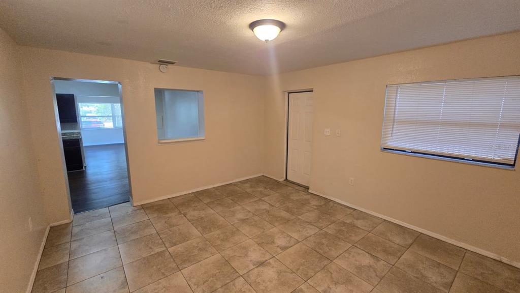 An empty room features beige walls, light-colored tile flooring, a ceiling light, and a window — 14857 SUNSET STREET, CLEARWATER, FL