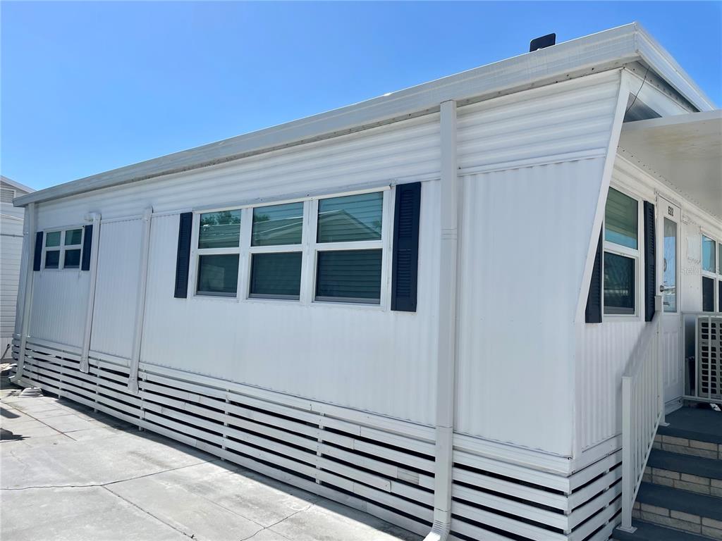 A white mobile home exterior features horizontal siding, dark shutters, and a concrete driveway — 3710 GULF OF MEXICO DRIVE UNIT E22, LONGBOAT KEY, FL