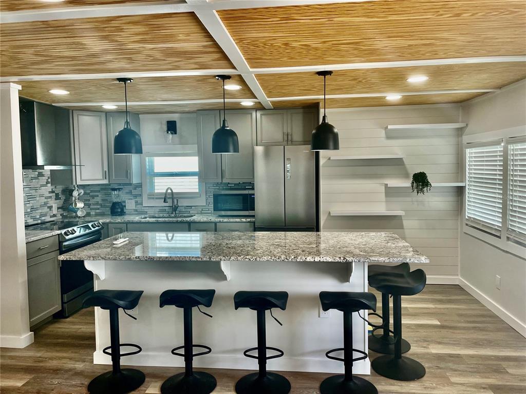 A kitchen features a granite-topped island, gray cabinetry, black pendant lights, and a wood-paneled ceiling — 3710 GULF OF MEXICO DRIVE UNIT E22, LONGBOAT KEY, FL