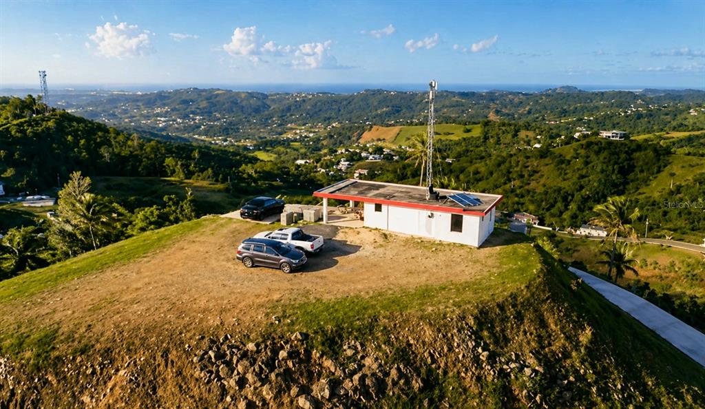 An aerial view shows a white building with a communications tower on a hilltop — LOMA DEL VIENTO BO. MASAS, GURABO, PR