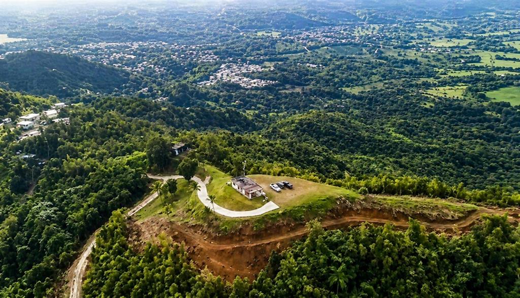 An aerial view shows a house on a hilltop surrounded by lush green forest — LOMA DEL VIENTO BO. MASAS, GURABO, PR