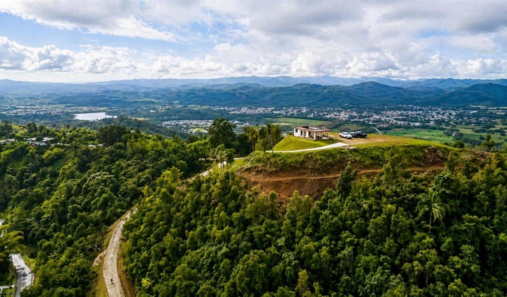 An aerial view shows a house situated on a grassy hilltop overlooking a valley — LOMA DEL VIENTO BO. MASAS, GURABO, PR