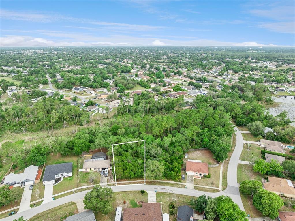 An aerial view shows a vacant, wooded residential lot outlined in white between two houses — 1672 GREGORY DRIVE, DELTONA, FL