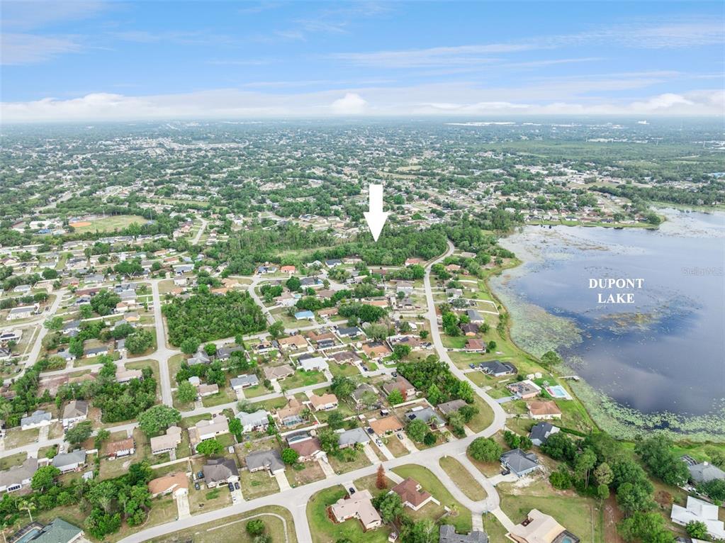 An aerial view shows a residential neighborhood near Dupont Lake with a white arrow pointing down — 1672 GREGORY DRIVE, DELTONA, FL