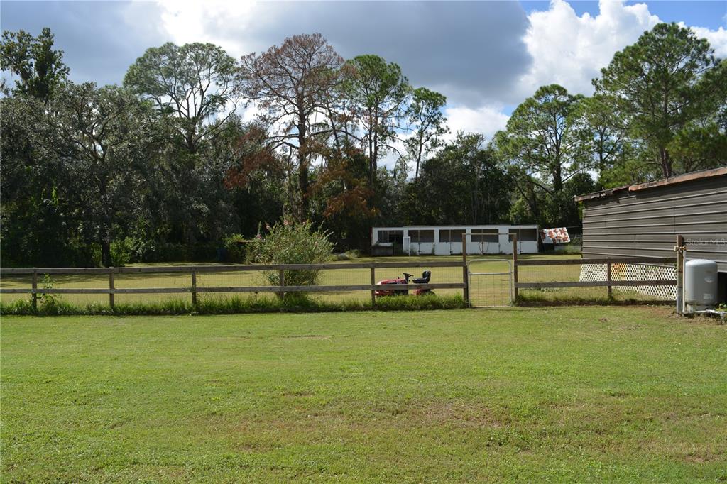 A grassy backyard features a wooden fence, a red riding lawnmower, and a small stable — 4424 ROSE STREET, VALRICO, FL