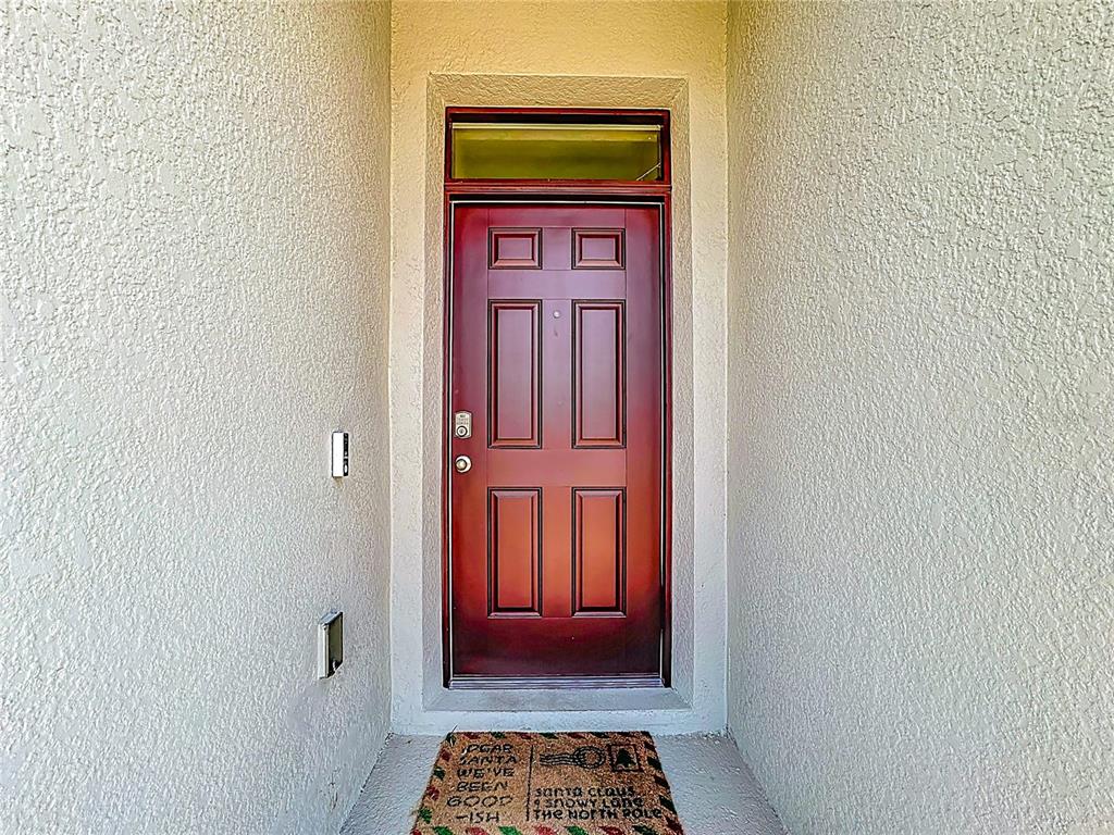 A red front door with a transom window sits in a stucco entryway — 1519 WAX MYRTLE WAY, HAINES CITY, FL