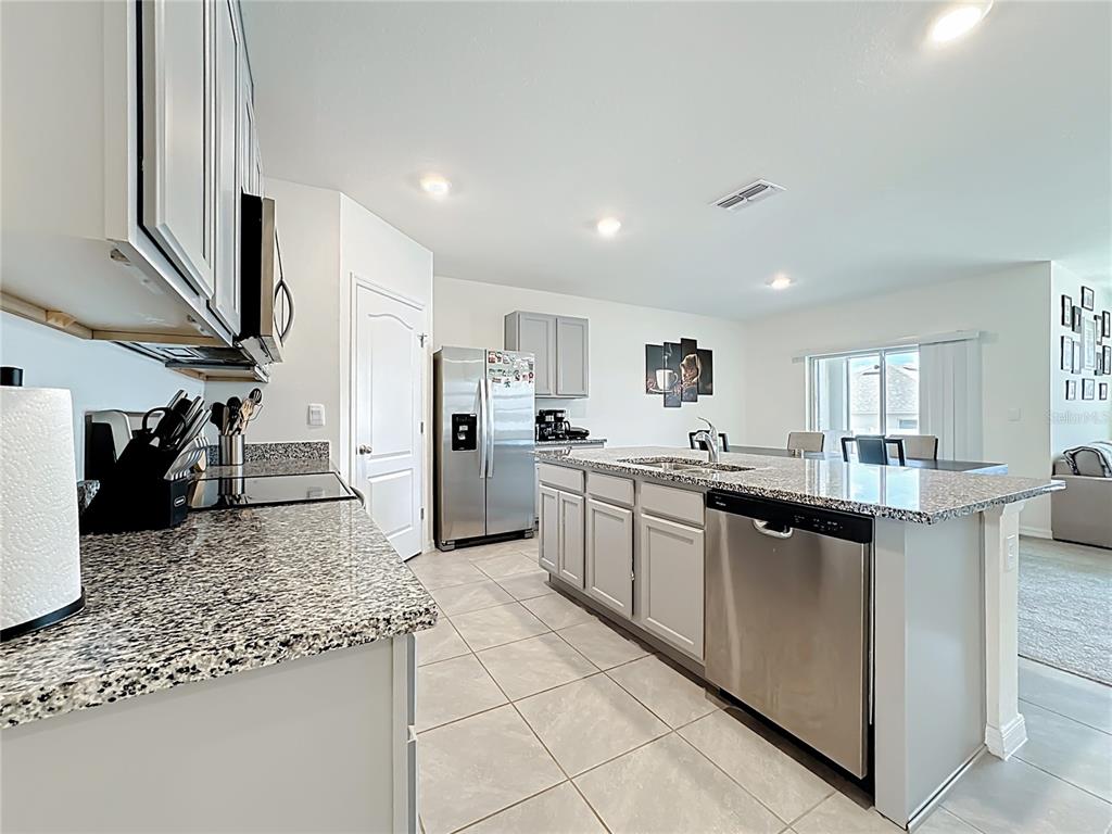 A modern kitchen features gray cabinets, granite countertops, stainless steel appliances, and tile flooring — 1519 WAX MYRTLE WAY, HAINES CITY, FL