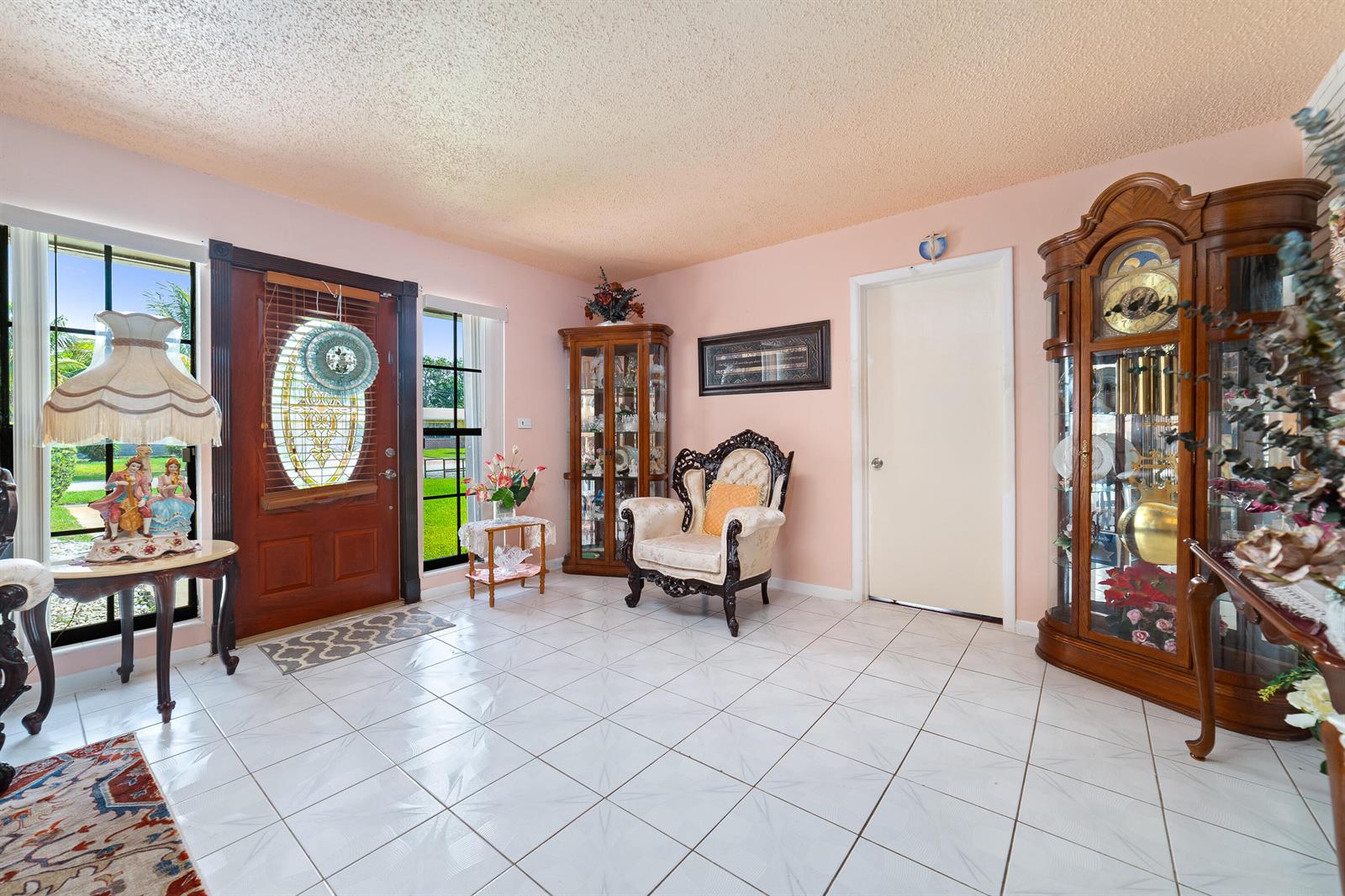 An entryway with light pink walls, white tile flooring, a wooden door, and antique-style furniture — 4460 NW 3rd Place, Plantation FL 33317, PLANTATION, FL