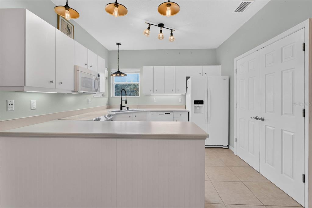 A kitchen features white cabinets, light-colored countertops, a white refrigerator, and multiple hanging light fixtures — 31 MAGNOLIA DRIVE S, ORMOND BEACH, FL