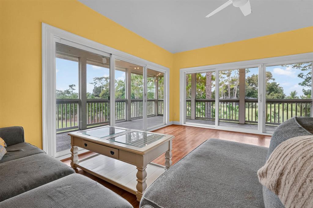 A sunroom with yellow walls, wood flooring, and sliding glass doors overlooking a wooded area — 31 MAGNOLIA DRIVE S, ORMOND BEACH, FL