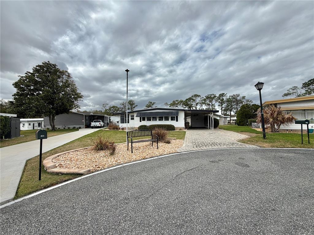 A single-story mobile home features a paved driveway, a carport, and a landscaped front yard — 104 DOGWOOD TRAIL, LEESBURG, FL