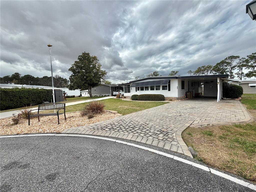 A single-story manufactured home features a paved driveway, a carport, and a front yard bench — 104 DOGWOOD TRAIL, LEESBURG, FL