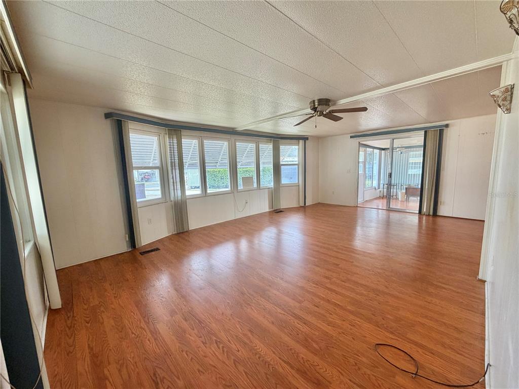 A spacious living room features wood-look flooring, a ceiling fan, and large windows — 104 DOGWOOD TRAIL, LEESBURG, FL