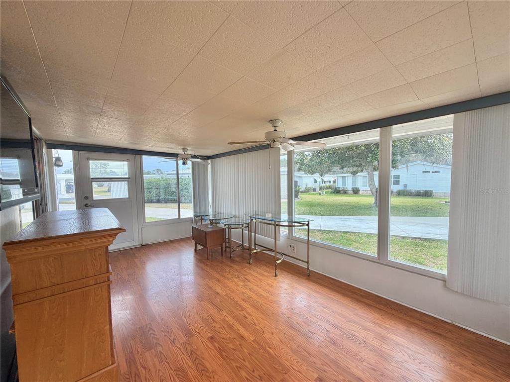 A sunroom with wood-look flooring, ceiling fans, and large windows overlooking a grassy yard — 104 DOGWOOD TRAIL, LEESBURG, FL