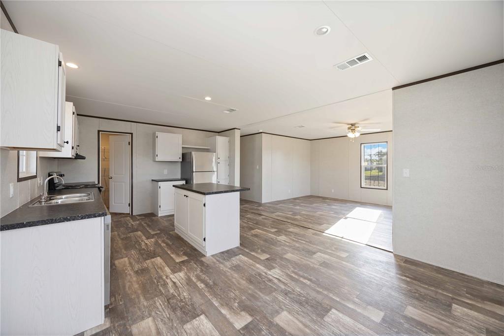 An open-concept kitchen and living area featuring white cabinets, a center island, and wood-look flooring — 4780 DUNCAN ROAD, PUNTA GORDA, FL