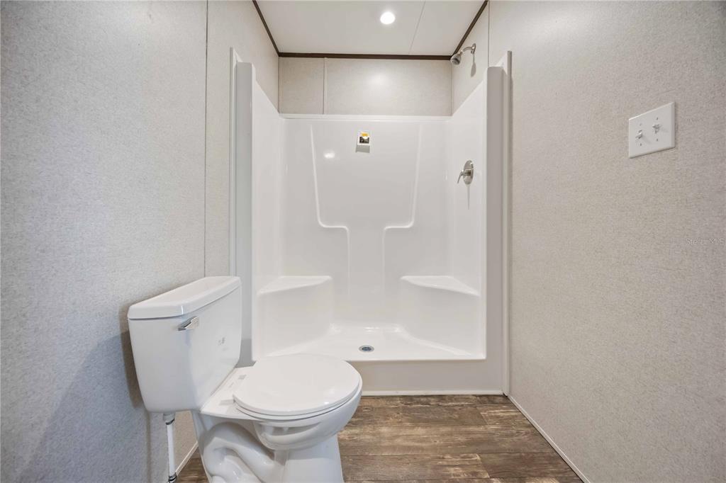 A bathroom features a white toilet, a walk-in shower with built-in seats, and wood-look flooring — 4780 DUNCAN ROAD, PUNTA GORDA, FL