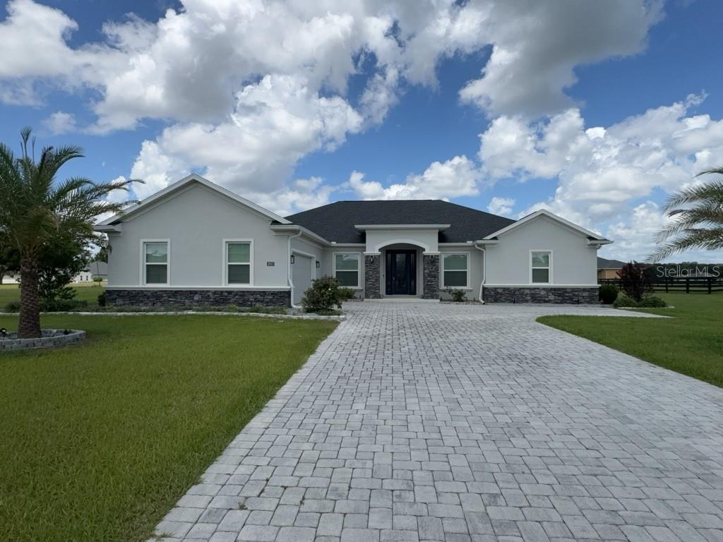 A single-story house with a stone-accented facade, gray stucco walls, and a paved driveway — 1817 NW 83RD LOOP, OCALA, FL