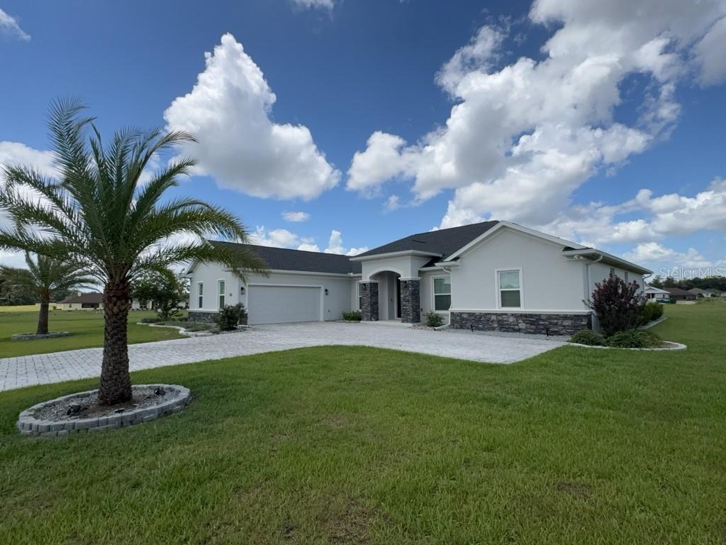 A single-story house with a white stucco exterior, stone accents, and a paved driveway — 1817 NW 83RD LOOP, OCALA, FL