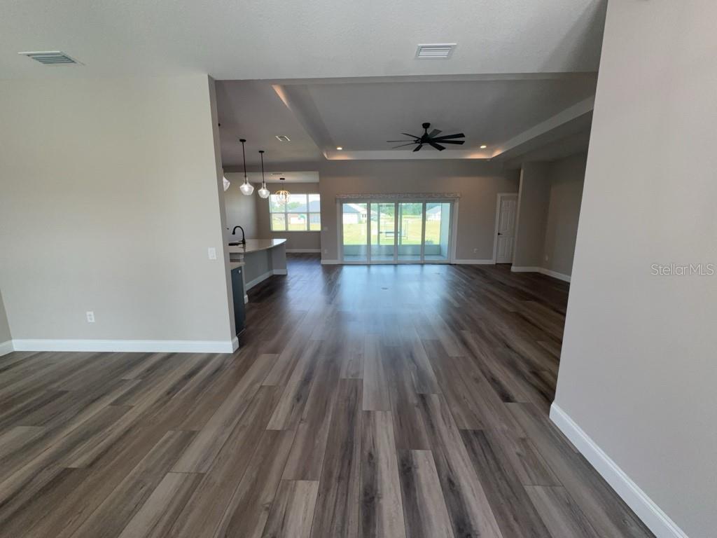An open-concept living area features wood-look flooring, a tray ceiling, and sliding glass doors — 1817 NW 83RD LOOP, OCALA, FL