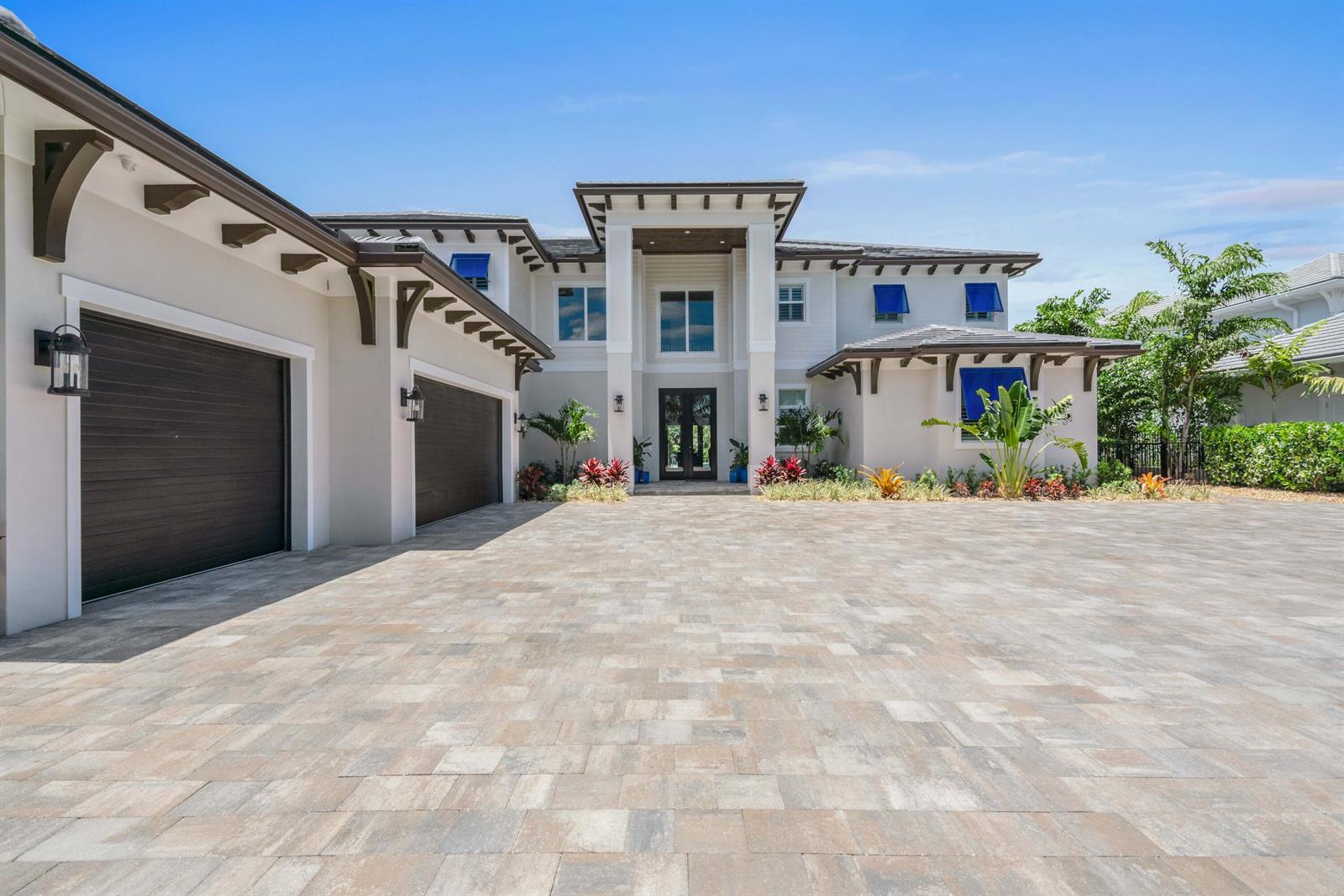 A two-story house with a large paved driveway, dark garage doors, and blue window awnings — 261 Old Jupiter Beach Road, Jupiter FL 33477, JUPITER, FL