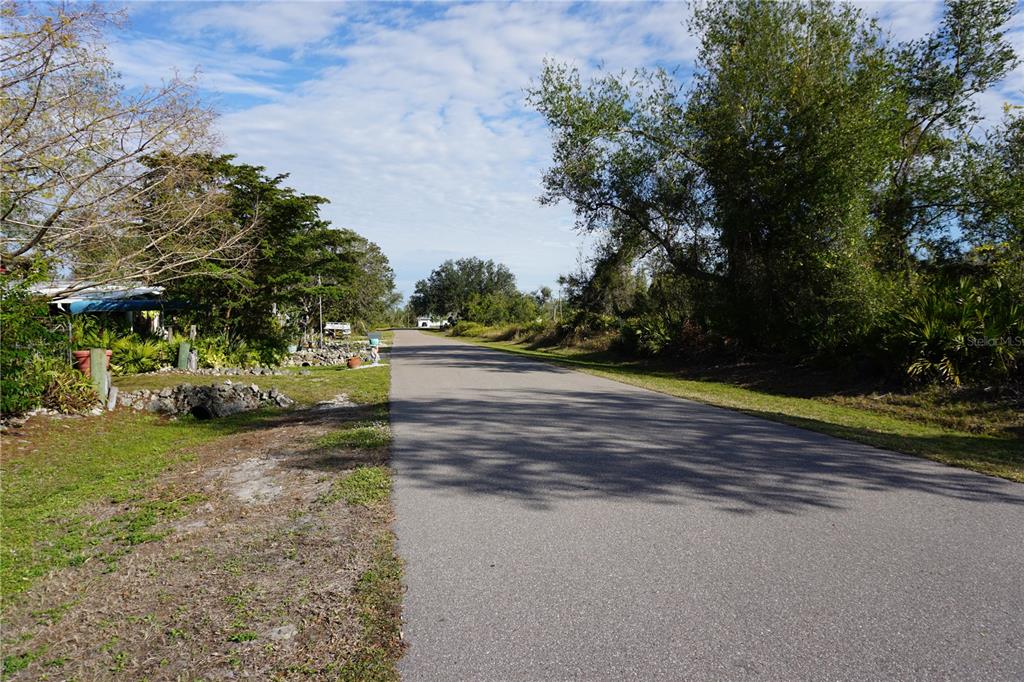 A paved road stretches into the distance, flanked by trees and vegetation on both sides — 334 OMEN STREET, PUNTA GORDA, FL