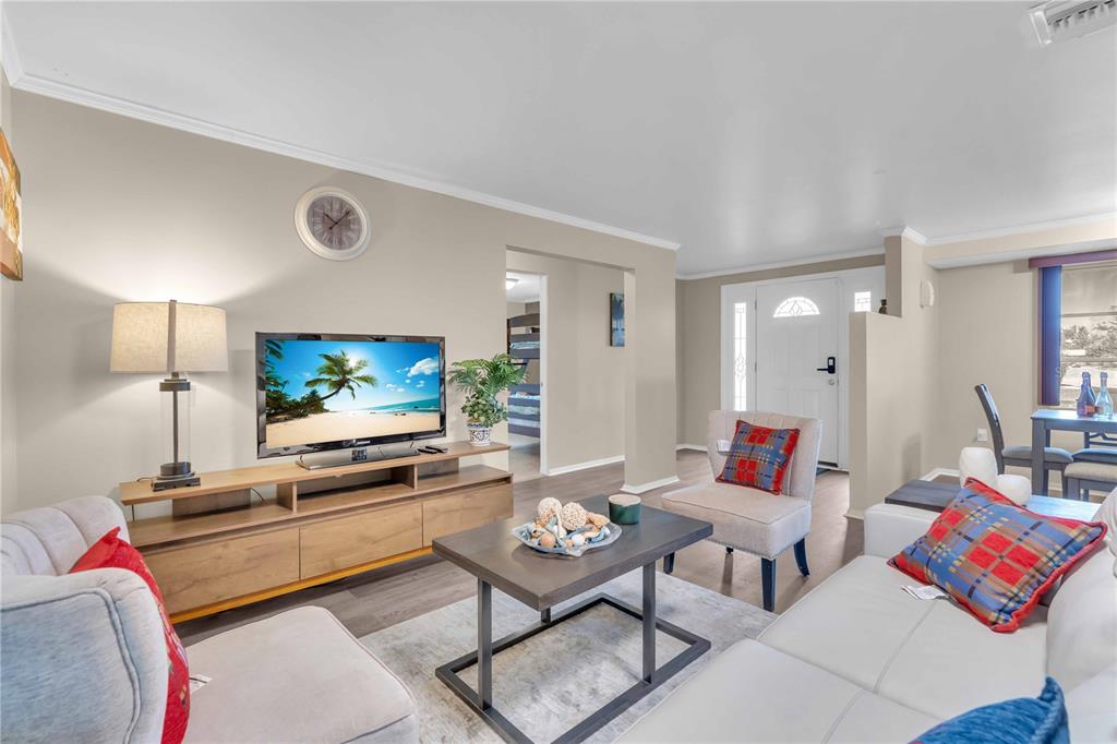 A living room features light-colored walls, wood-look flooring, a television console, and white furniture — 7420 CASS CIRCLE, SARASOTA, FL