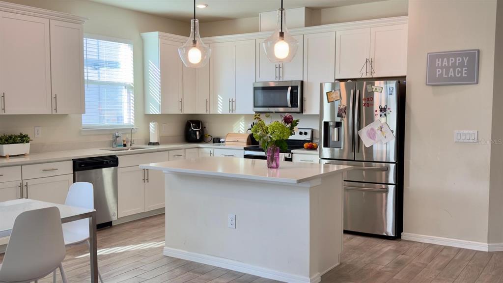 A kitchen features white cabinets, stainless steel appliances, a center island, and wood-look flooring — 4620 GLIDING WAVE ST, WINTER GARDEN, FL