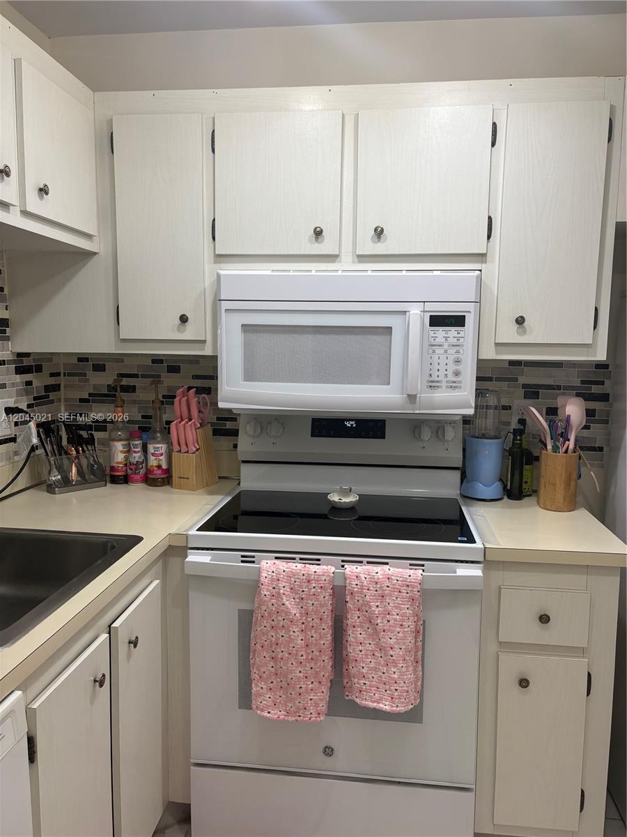 A kitchen features white cabinets, a glass-top stove, a microwave, and a tiled backsplash — 9340 Lagoon Pl # 202, Davie FL 33324, DAVIE, FL