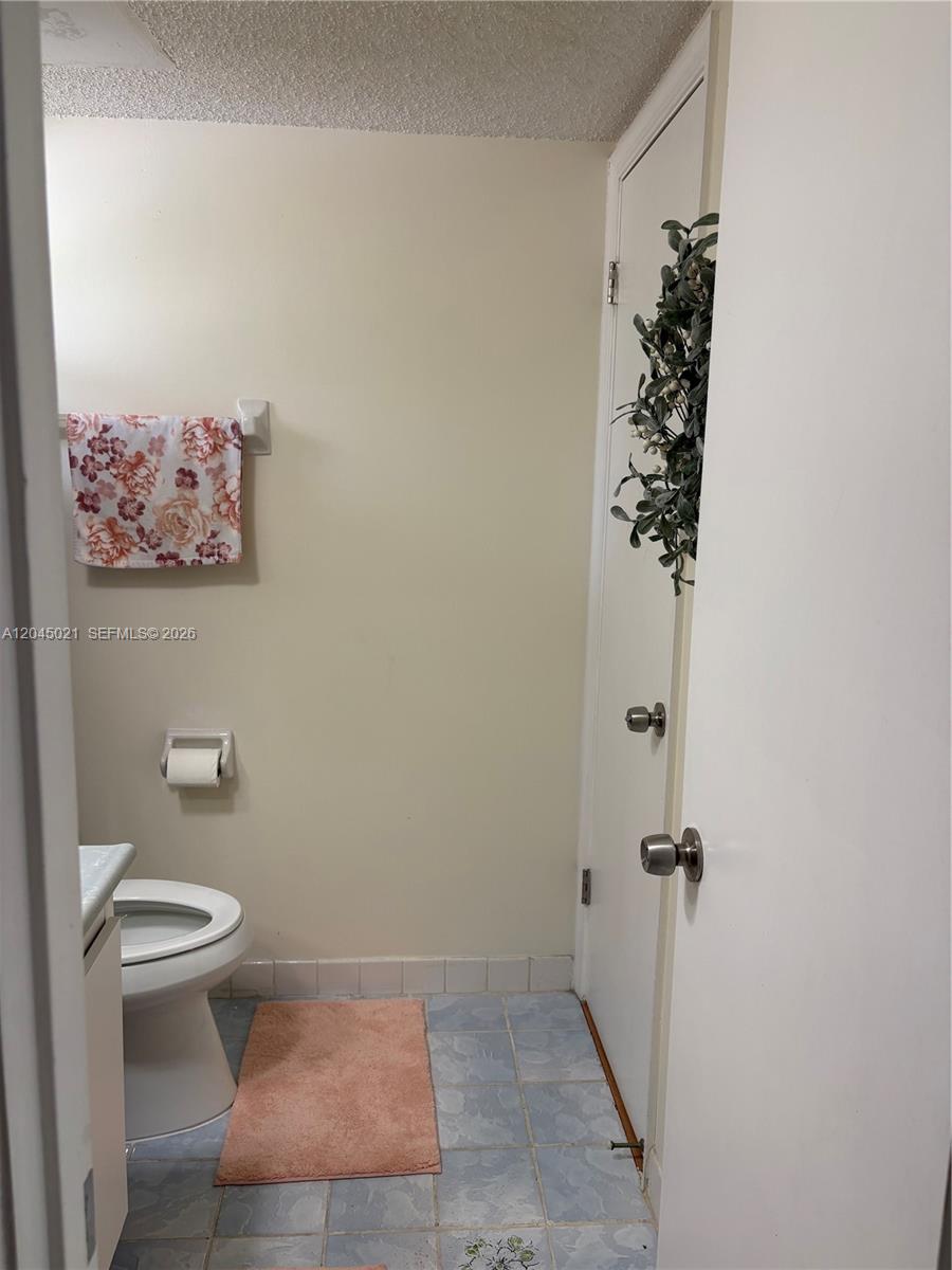 A small bathroom features a toilet, a floral hand towel, and light blue tiled flooring — 9340 Lagoon Pl # 202, Davie FL 33324, DAVIE, FL