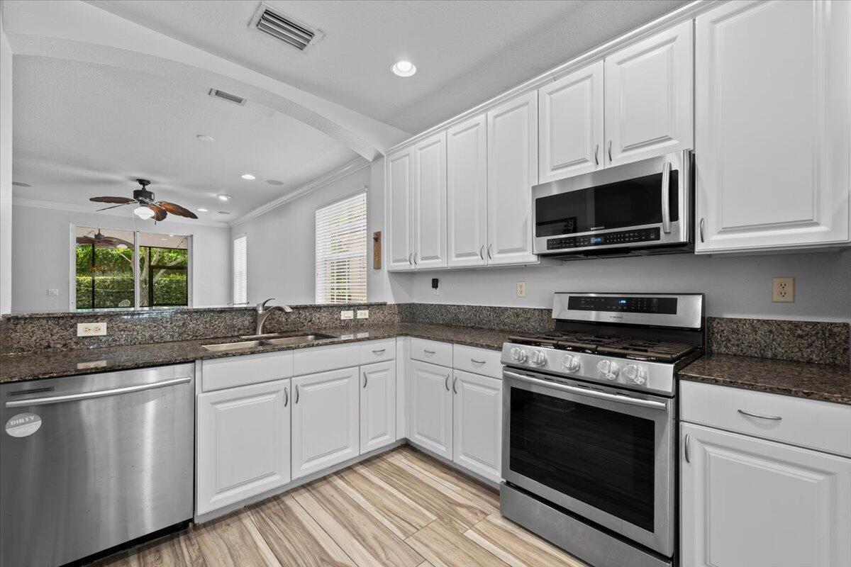A kitchen features white cabinets, granite countertops, stainless steel appliances, and wood-look tile flooring — 603 Castle Drive, Palm Beach Gardens FL 33410, PALM BEACH GARDENS, FL
