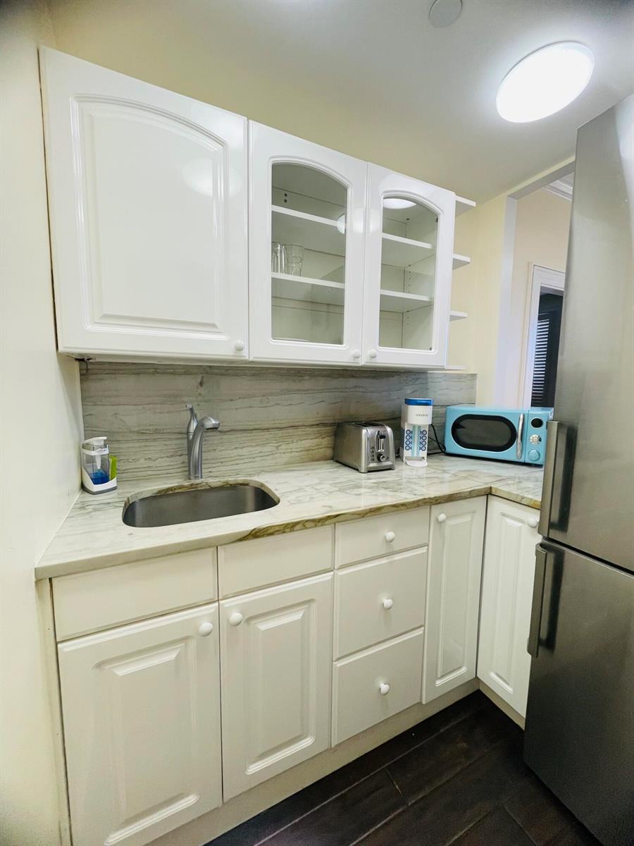 A small kitchen features white cabinets, a stone countertop, a stainless steel sink, and appliances — 235 Sunrise Avenue # 2262, Palm Beach FL 33480, PALM BEACH, FL