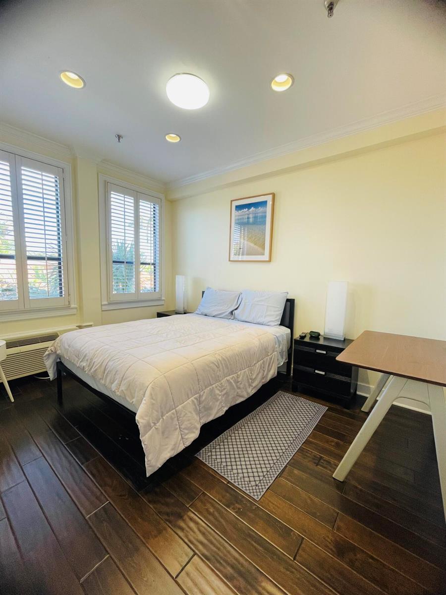 A bedroom features a bed with a white comforter, dark wood flooring, and plantation shutters — 235 Sunrise Avenue # 2262, Palm Beach FL 33480, PALM BEACH, FL