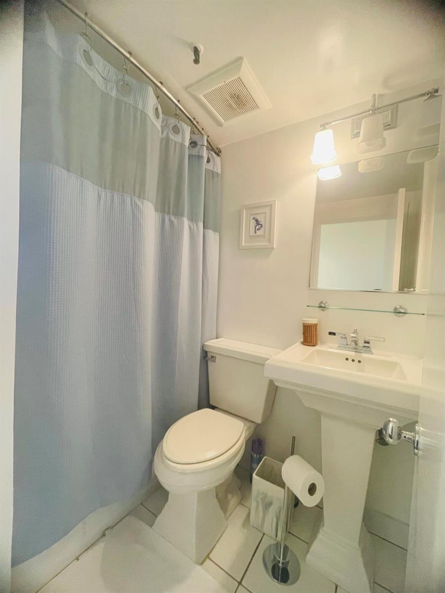 A small bathroom features a pedestal sink, a toilet, and a blue and white shower curtain — 235 Sunrise Avenue # 2262, Palm Beach FL 33480, PALM BEACH, FL