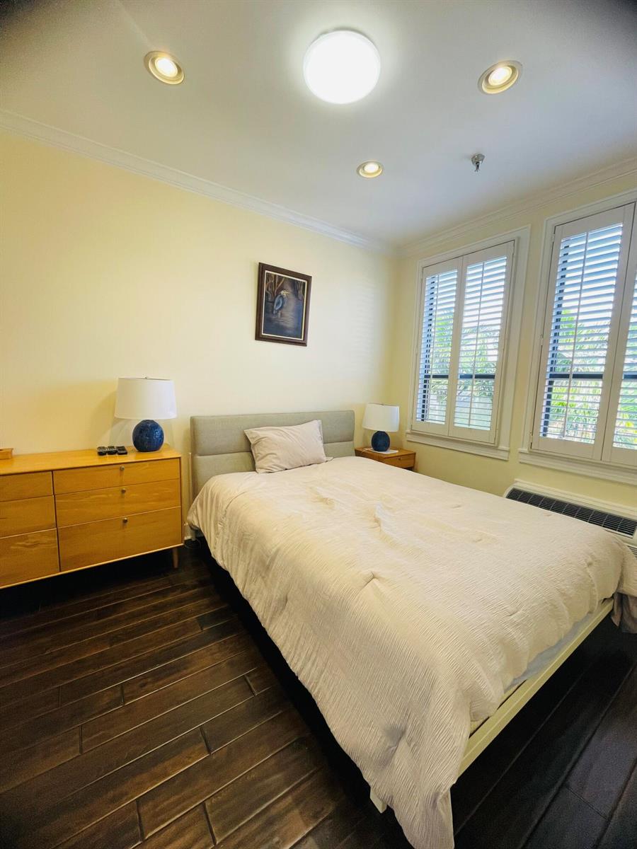 A bedroom features a bed, a wooden dresser, dark wood flooring, and plantation shutters — 235 Sunrise Avenue # 2262, Palm Beach FL 33480, PALM BEACH, FL