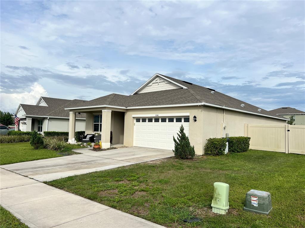 A single-story suburban house with a tan stucco exterior, a two-car garage, and a driveway — 5240 GREENHEART AVENUE, MOUNT DORA, FL
