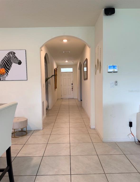 A tiled hallway leads to a white front door through a large arched entryway — 5240 GREENHEART AVENUE, MOUNT DORA, FL