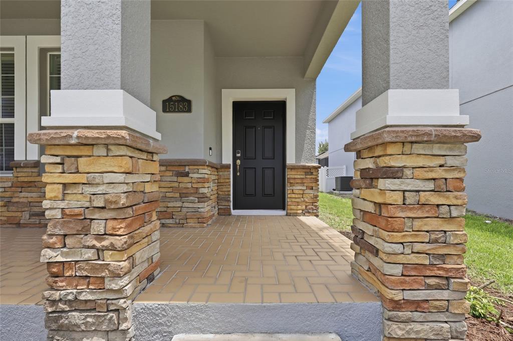 A covered front porch features stone-clad pillars, a paved floor, and a black front door — 15183 BRIDGEWATER CROSSINGS BOULEVARD, WINTER GARDEN, FL