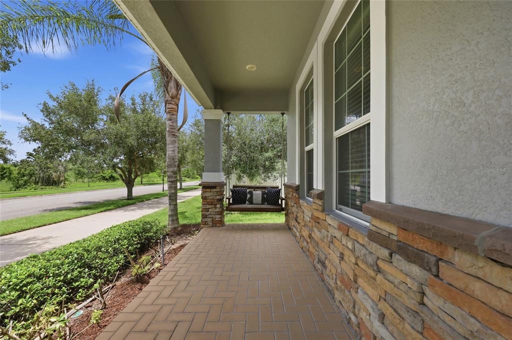 A covered front porch features a stone-accented wall, brick paver flooring, and a hanging swing — 15183 BRIDGEWATER CROSSINGS BOULEVARD, WINTER GARDEN, FL