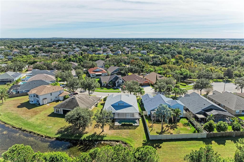 An aerial view shows a suburban neighborhood with houses, swimming pools, and a small pond — 7114 CROMWELL PARK LANE, APOLLO BEACH, FL
