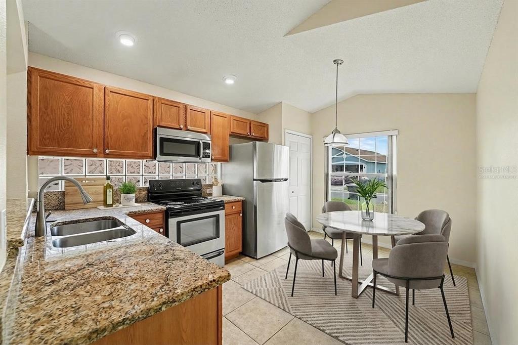 A kitchen with wood cabinets, granite countertops, stainless steel appliances, and a dining area — 162 CANARY ISLAND CIRCLE, DAVENPORT, FL