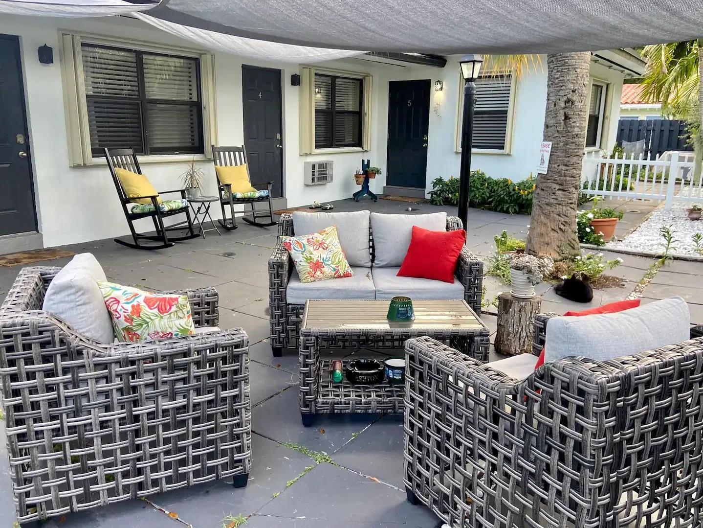 A patio area features gray wicker outdoor furniture, rocking chairs, and a white picket fence — 213 Hibiscus Avenue, Pompano Beach FL 33062, POMPANO BEACH, FL