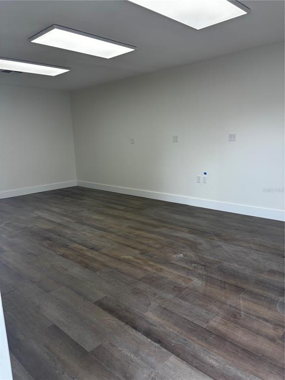An empty room features light gray walls, white baseboards, and dark wood-look flooring — 5417 GRAND BOULEVARD UNIT B, NEW PORT RICHEY, FL