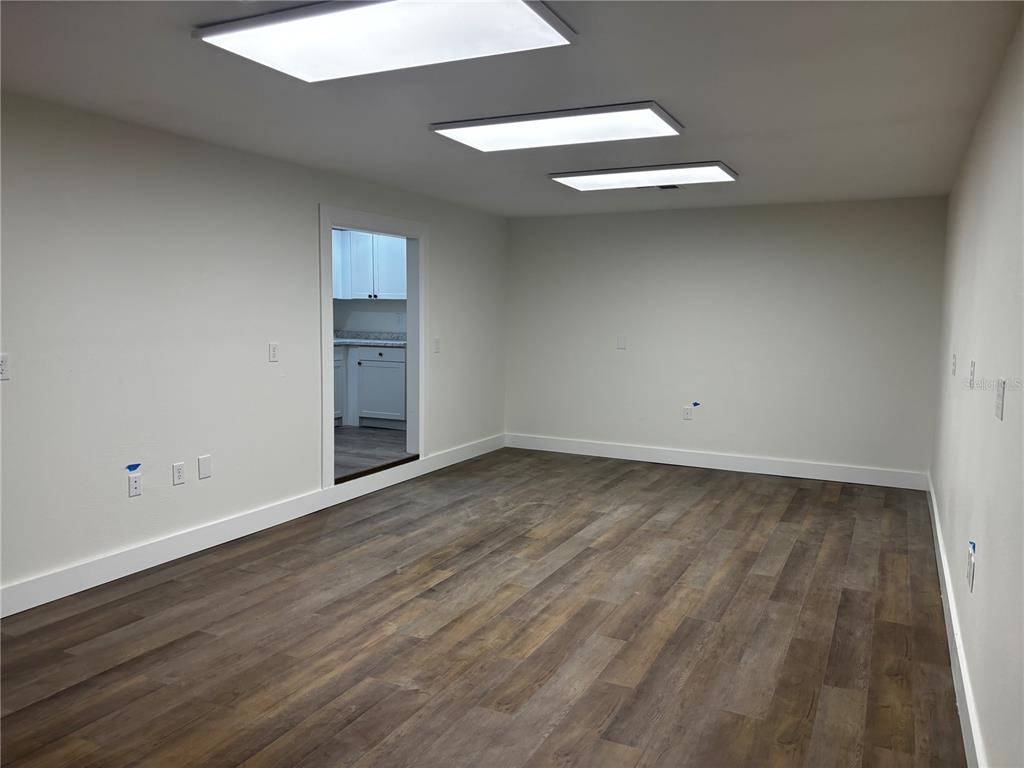 An empty room features wood-look flooring, white walls, and three rectangular ceiling light fixtures — 5417 GRAND BOULEVARD UNIT B, NEW PORT RICHEY, FL