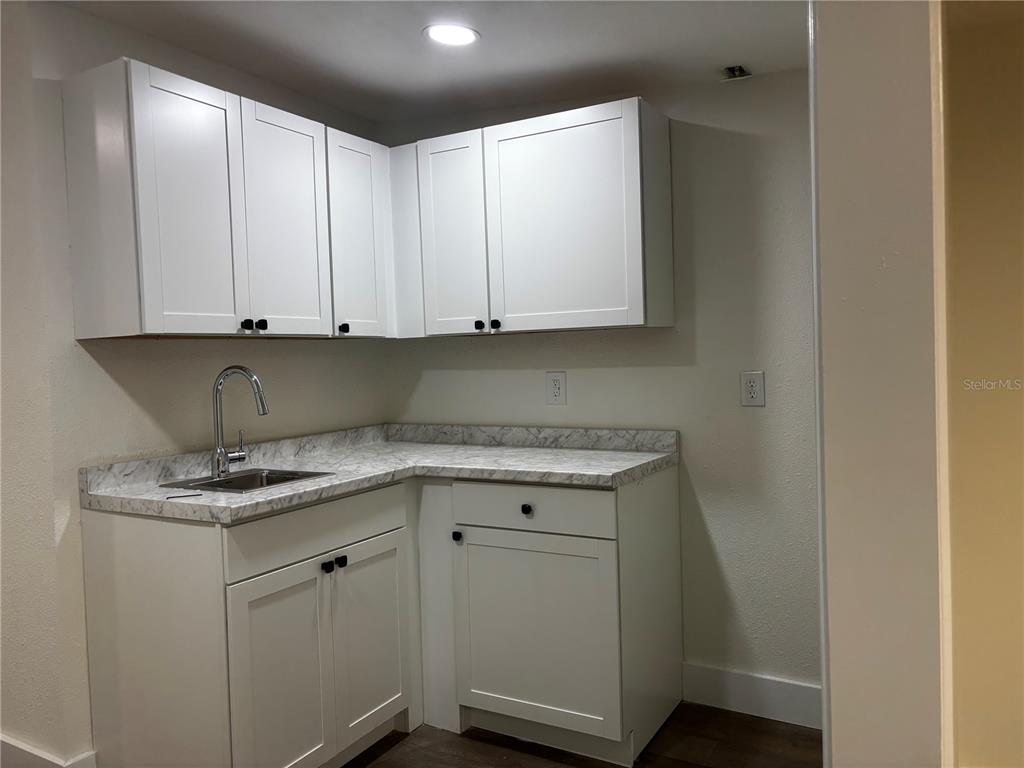 A small kitchen features white shaker cabinets, a marble-patterned countertop, and a stainless steel sink — 5417 GRAND BOULEVARD UNIT B, NEW PORT RICHEY, FL