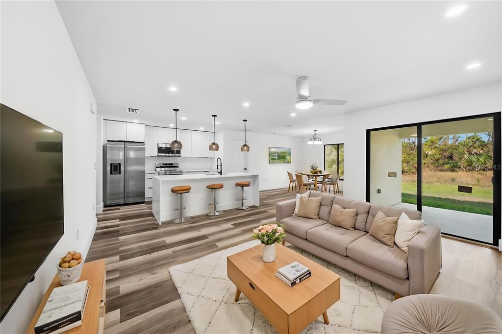 A bright open-concept living room and kitchen with wood-look flooring and sliding glass patio doors — 15468 CHAMBERLAIN BOULEVARD, PORT CHARLOTTE, FL