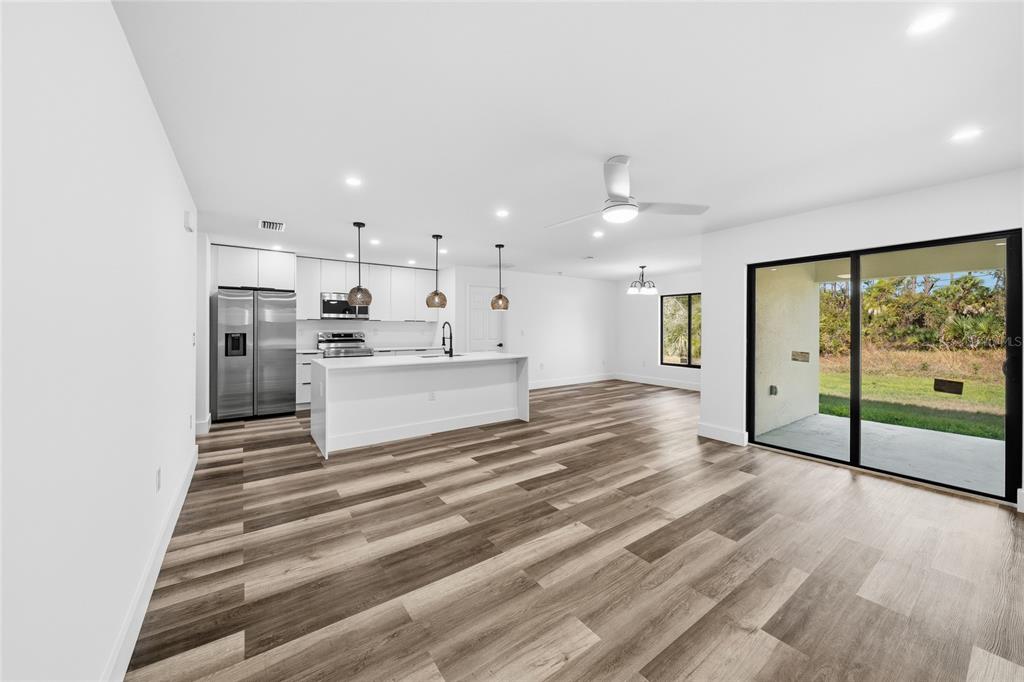 A modern open-concept kitchen and living area with white cabinetry, a kitchen island, and wood-look flooring — 15468 CHAMBERLAIN BOULEVARD, PORT CHARLOTTE, FL