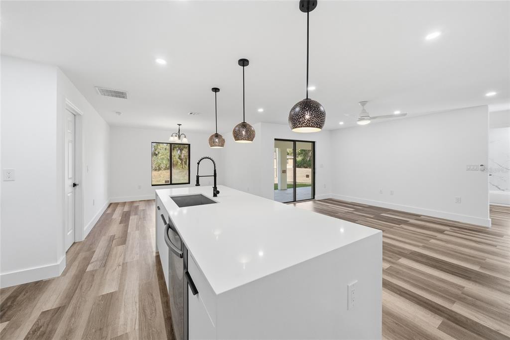 A modern kitchen features a white quartz island, pendant lighting, and wood-look flooring — 15468 CHAMBERLAIN BOULEVARD, PORT CHARLOTTE, FL
