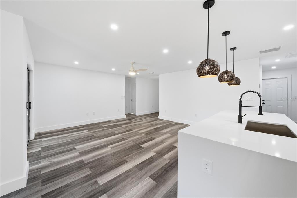 A modern kitchen island with a sink overlooks an open-concept living area with wood-look flooring — 15468 CHAMBERLAIN BOULEVARD, PORT CHARLOTTE, FL