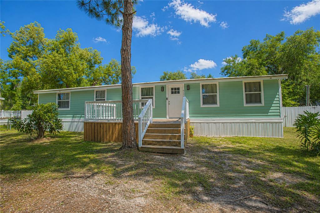 A light green mobile home with a wooden deck and stairs sits on a grassy lot — 5175 COUNTRYSIDE COURT, ST CLOUD, FL