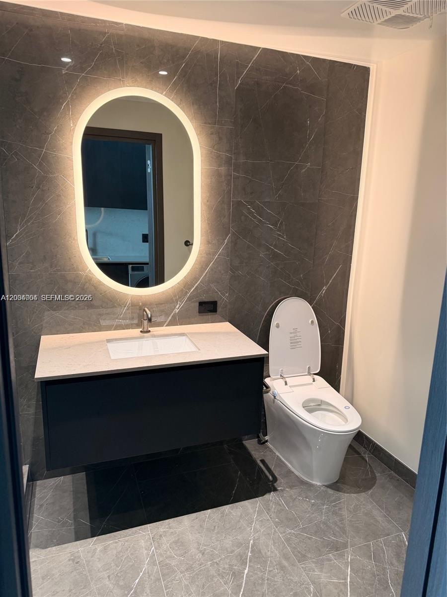 A modern bathroom features a floating vanity, an oval backlit mirror, and dark marble tiling — 20 NE 11th St # 3703A, Miami FL 33132, MIAMI, FL